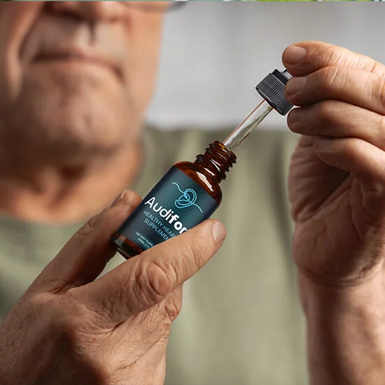 A hand holding an Audifort bottle with the dropper lifted out, ready for a daily serving
